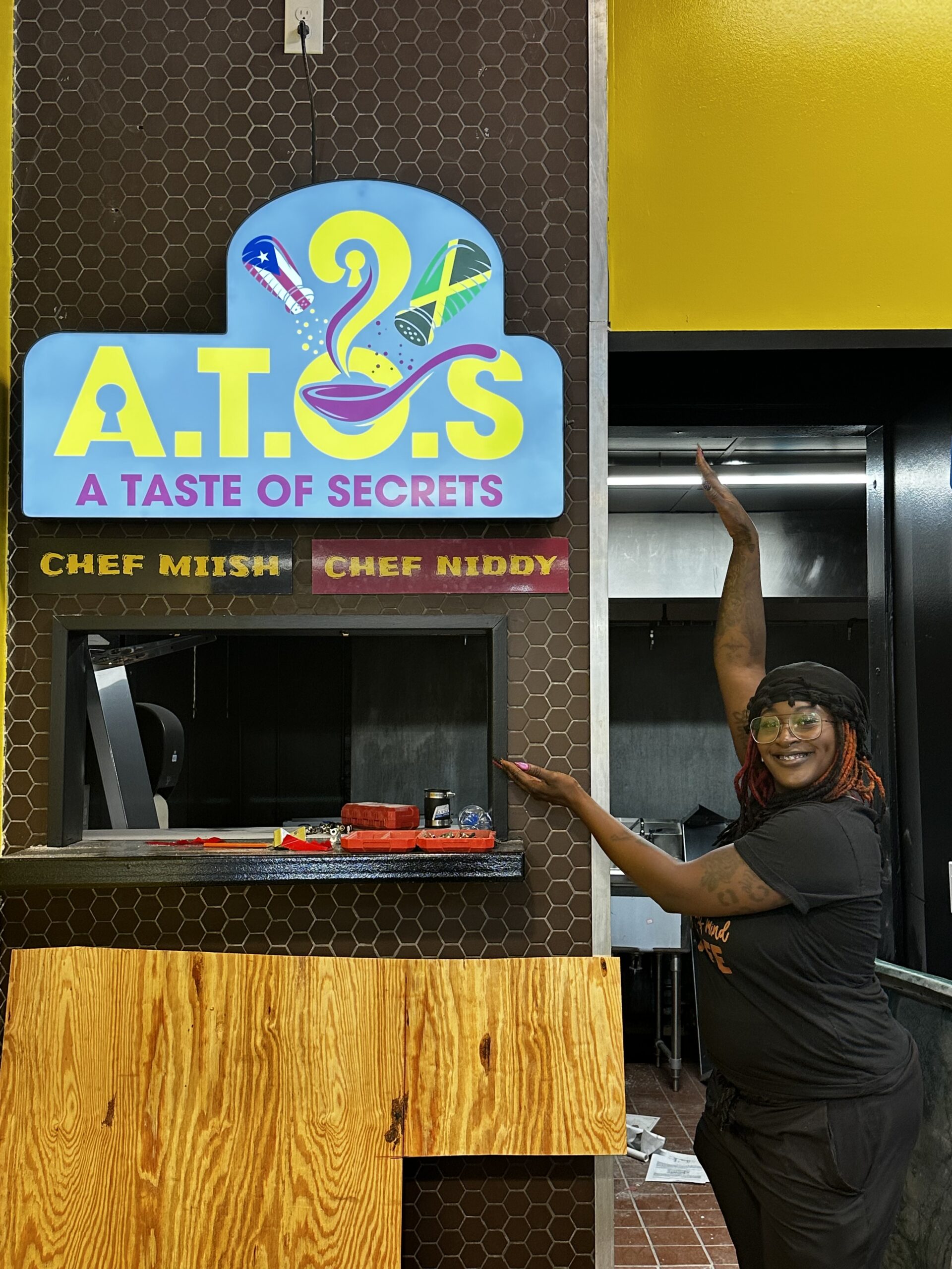 Illuminated light box sign for A Taste of Secrets in Atlanta, GA, featuring bright, colorful branding above the service window in a busy market setting